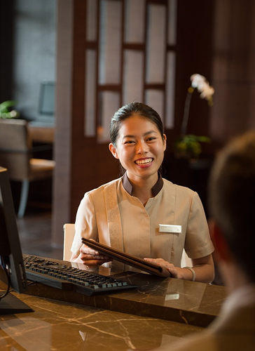 A Chinese receptionist sitting at a computer and motioning toward a folio